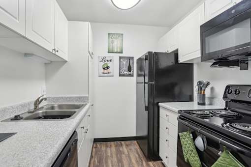A black refrigerator sits in a kitchen with white cabinets. at Millennium at Creve Coeur, Missouri