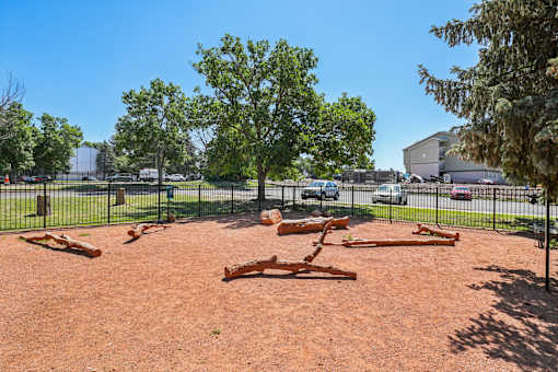 A playground with a red dirt surface and a black fence.