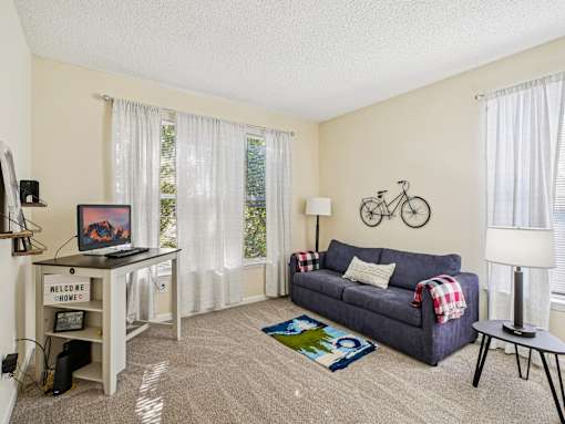 A living room with a couch, a table, and a bicycle on the wall. at Cedar Springs Apartments, Raleigh, NC