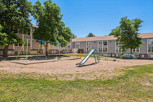 A playground with a slide and swings in front of a building.