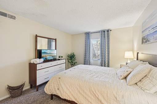 A bedroom with a large bed, a dresser, and a mirror. at Sarasota South Apartments, Bradenton, 34207