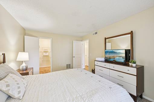 A bedroom with a large bed, a dresser with a mirror, and a lamp on a nightstand. at Sarasota South Apartments, Bradenton, FL