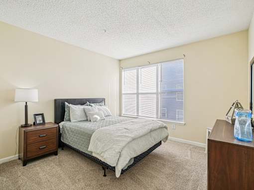 A bedroom with a bed, nightstand, and window. at Cedar Springs Apartments, Raleigh, NC, 27609