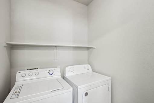 Two white front loading washing machines in a small laundry room at Sweetwater At Metro North Apartments, Phoenix, AZ 85029