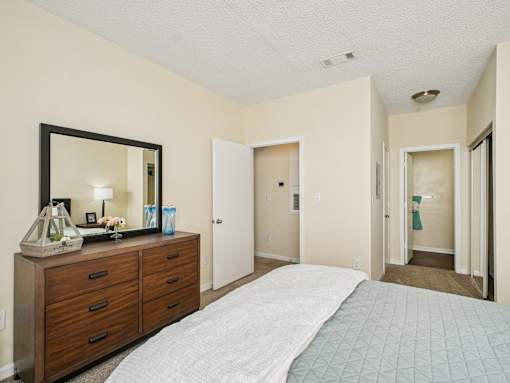 A bedroom with a bed, dresser, mirror, and two doors. at Cedar Springs Apartments, North Carolina, 27609
