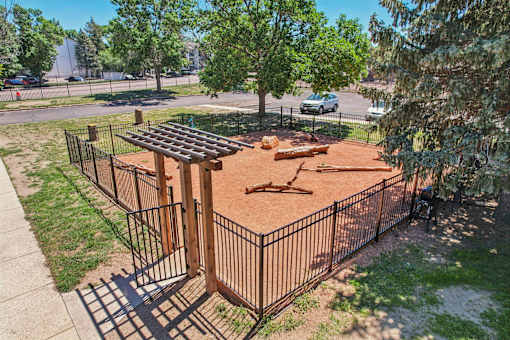 A playground with a brown surface and a black fence.