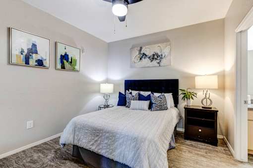 A bedroom with a bed, nightstand, and two wall art pieces at Sweetwater At Metro North Apartments, Phoenix, AZ 85029