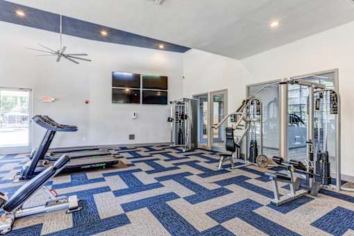 A spacious gym with a variety of equipment and a blue and white patterned carpet at Sweetwater At Metro North Apartments, Phoenix