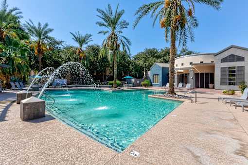 A pool with a waterfall and palm trees in the background at Sweetwater At Metro North Apartments, Arizona 85029