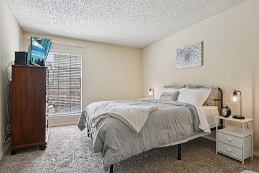 A bedroom with a bed, nightstand, and window with blinds.