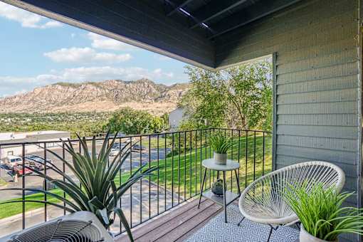 A balcony with a chair and a table overlooking a parking lot and a mountain at Cliffs at Canyon Ridge, Ogden, UT, 84401