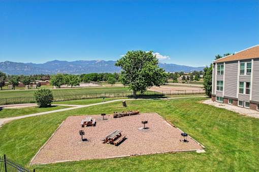 A park area with picnic tables and benches in the foreground and a building in the background.