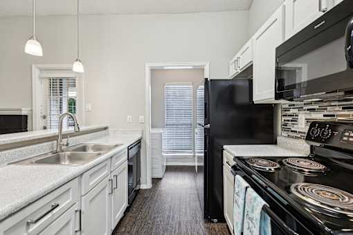 A black refrigerator sits in a kitchen with white cabinets and a black stove.