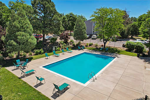 A swimming pool surrounded by green trees and lawn chairs.
