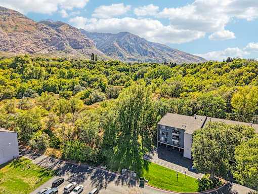 A building is surrounded by a green landscape and a mountain in the background at Cliffs at Canyon Ridge, Ogden, UT, 84401