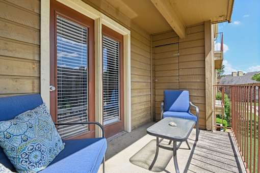 A blue couch with a decorative pillow sits on a porch with a small table and chair.