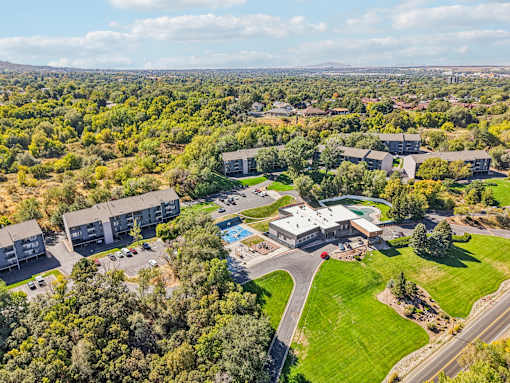 A bird's eye view of a residential area with houses, a swimming pool, and a road at Cliffs at Canyon Ridge, Ogden, UT, 84401