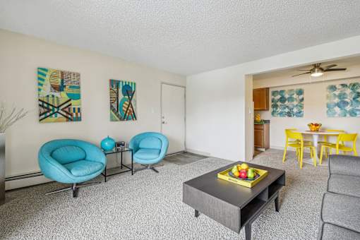 A living room with a grey sofa, a blue chair, a yellow chair, and a table with a bowl of fruit on it at Spyglass Creek, Denver, 80224