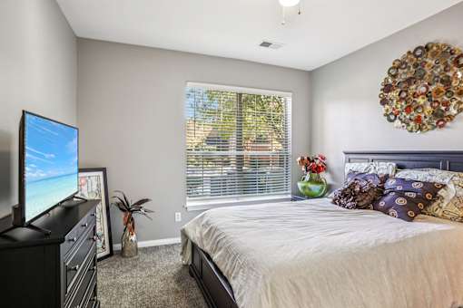 A bedroom with a large bed, a television, and a window with blinds. at Bridford Lake Apartments, Greensboro, NC, 27407