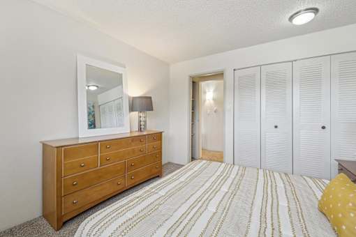 A bedroom with a wooden dresser and a striped bedspread at Spyglass Creek, Denver, 80224
