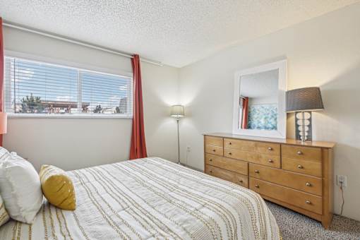 A bedroom with a bed, dresser, and window with red curtains at Spyglass Creek, Denver, 80224