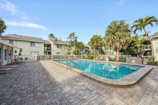 A swimming pool surrounded by a brick patio and palm trees. at Sarasota South Apartments, Bradenton, FL, 34207