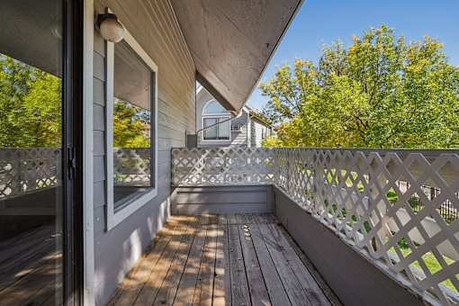 A wooden deck with a lattice fence and a view of a house and trees. at Windmill Apartments, Colorado, 80916