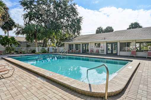 A swimming pool surrounded by a brick patio and a building in the background. at Sarasota South Apartments, Bradenton, FL