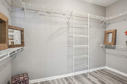 A walk-in closet with white shelving and a mirror on the wall. at Bridford Lake Apartments, Greensboro