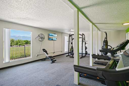 A gym with a row of treadmills and a fan on the wall.