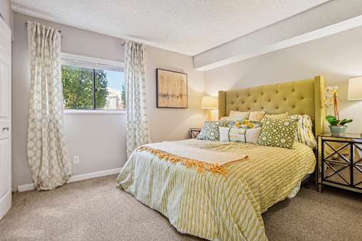 A bedroom with a large bed and a window with curtains. at Deer Crest Apartments, Broomfield, Colorado