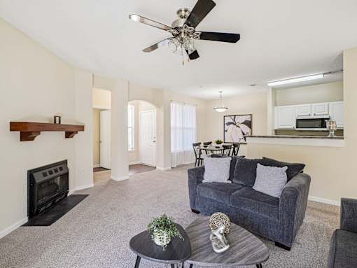 A living room with a grey couch, a black fireplace, and a ceiling fan. at Cedar Springs Apartments, Raleigh