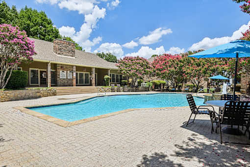 A pool surrounded by chairs and a house with a stone wall.