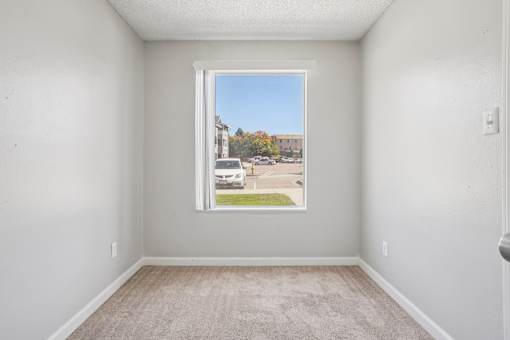 A room with a carpeted floor and a window showing a street view. at Windmill Apartments, Colorado Springs, 80916