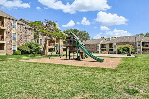 A playground with a green slide and a wooden swing set.