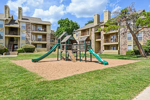 A playground with a green slide in front of apartment buildings.