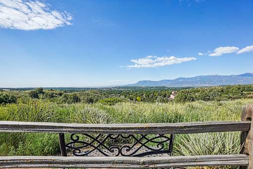 A bench with a metal frame overlooks a grassy field with mountains in the distance.