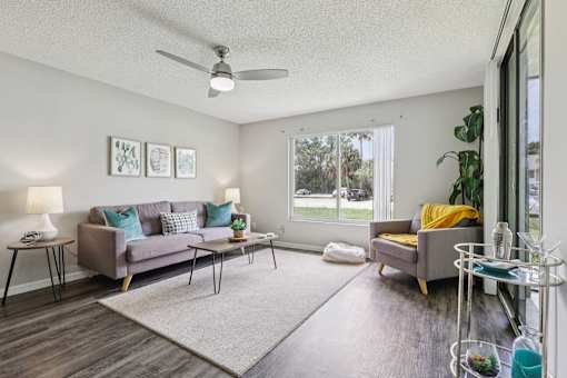 A living room with a grey couch, a yellow chair, and a white ceiling fan. at Lakeside Glen Apartments, Melbourne, Florida