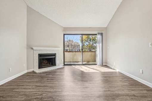 A large, empty room with a fireplace and sliding glass doors leading to a balcony. at Deer Crest Apartments, Broomfield, CO, 80020