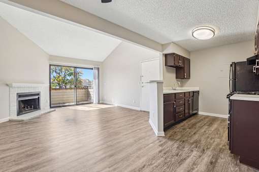 A living room with a fireplace and a kitchen area with brown cabinets. at Deer Crest Apartments, Broomfield, CO