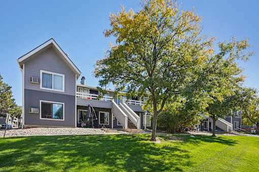 A grey house with a tree in front of it. at Windmill Apartments, Colorado Springs, Colorado