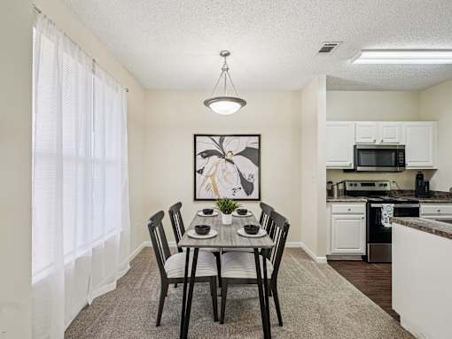 A dining room with a table set for two and a kitchen in the background. at Cedar Springs Apartments, Raleigh, NC, 27609