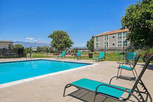 A swimming pool surrounded by lawn chairs and trees.