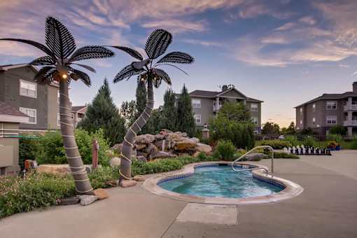 a swimming pool with palm trees in front of apartment buildings at Heritage at Stone Mountain, Northglenn, CO, 80233