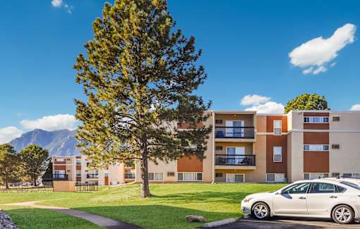A white car is parked in front of a building with a tree in the foreground at Broadmoor Springs, Colorado Springs, CO, 80906