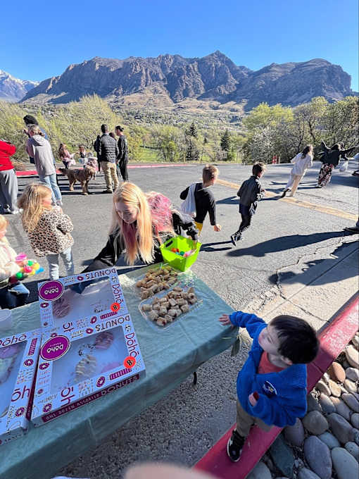 A child in a blue jacket is reaching for a snack on a table with a mountain in the background at Cliffs at Canyon Ridge, Ogden, UT, 84401
