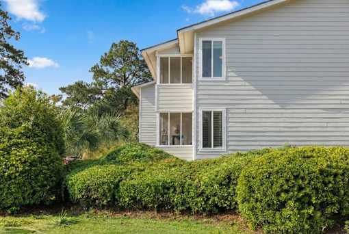 A house with a grey siding and a white window is surrounded by green bushes at River Crossing Apartments, Thunderbolt