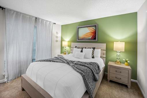 Furnished bedroom with green accent wall and white bedding and curtains at University Ridge Apartments, Durham, NC, 27707