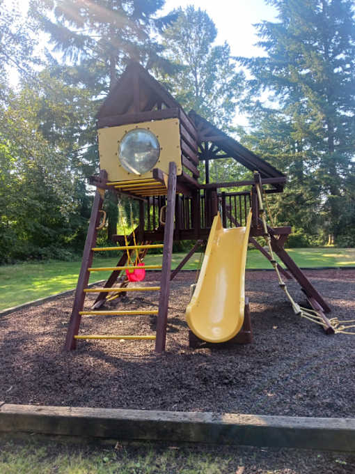 A playground with a yellow slide and a brown roof.
