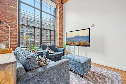 a living room with a large window and a couch and a chair at Riverwalk Apartments, Lawrence, MA